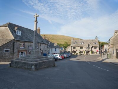 Picturesque street view in Corfe Castle, England, showcasing stone buildings and a historical monument.